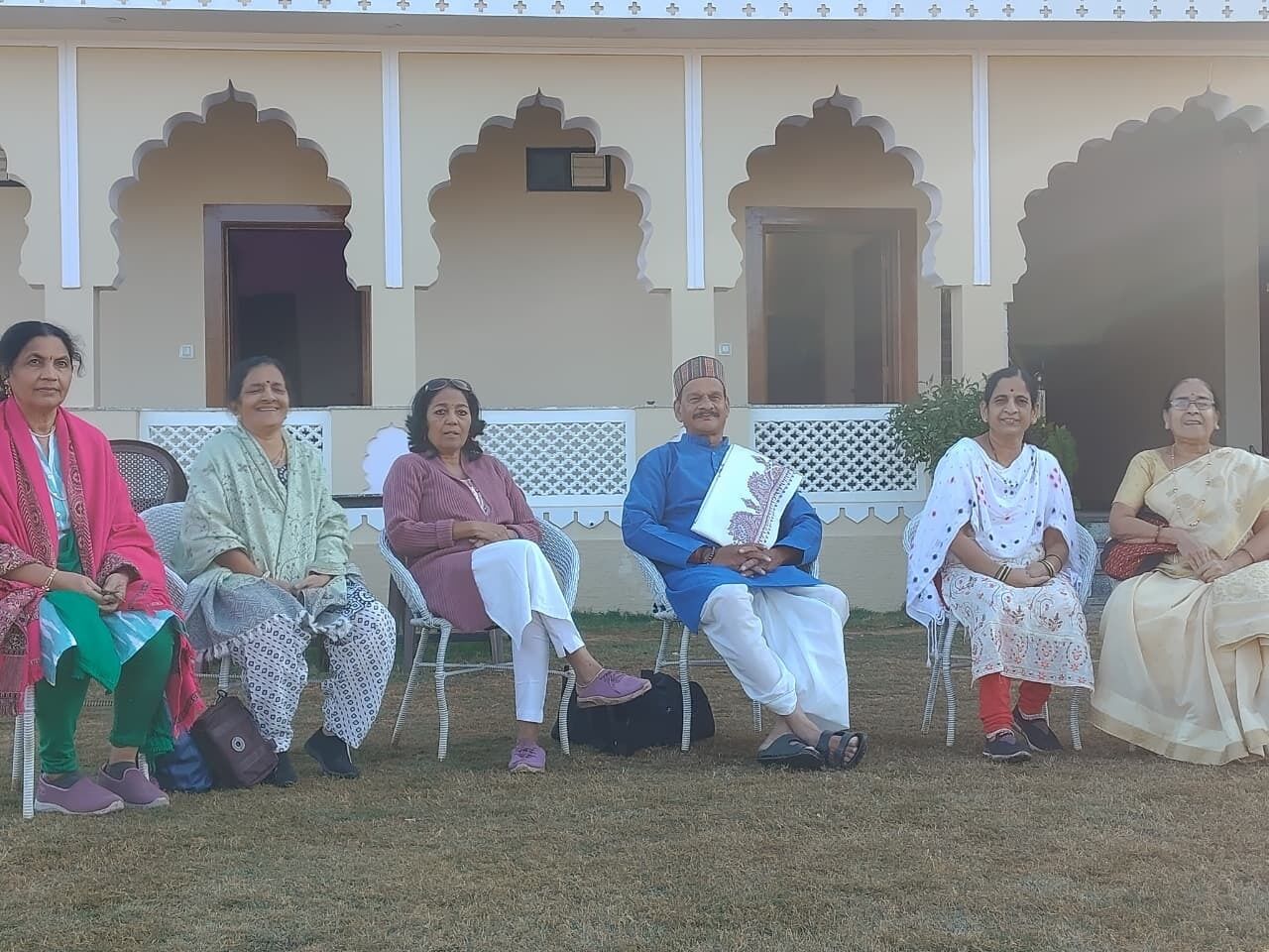 A group of people seated outdoors in front of a building with traditional architecture.
