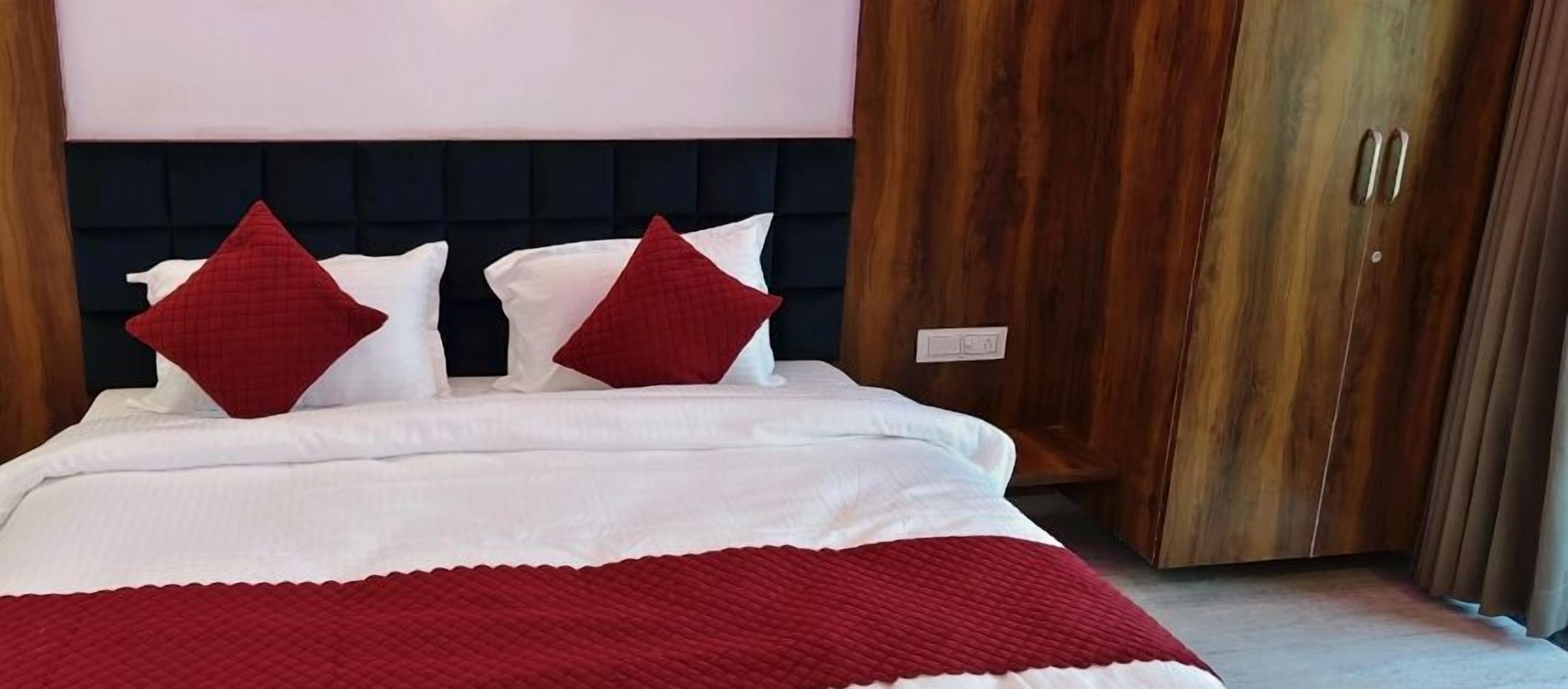 A bed with white bedding and red pillows, a dark headboard, and wooden wardrobe doors.