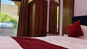 Une chambre d’hôtel avec un lit, un oreiller rouge et une vue sur un paysage montagneux par la fenêtre.