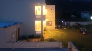Un bâtiment moderne doté de nombreuses fenêtres illuminées et d’une piscine en premier plan.