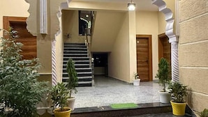 Un escalier menant à une porte sur laquelle est posé un paillasson avec l’inscription « BIENVENUE », le tout étant entouré de plantes en pot et d’une caméra de surveillance.