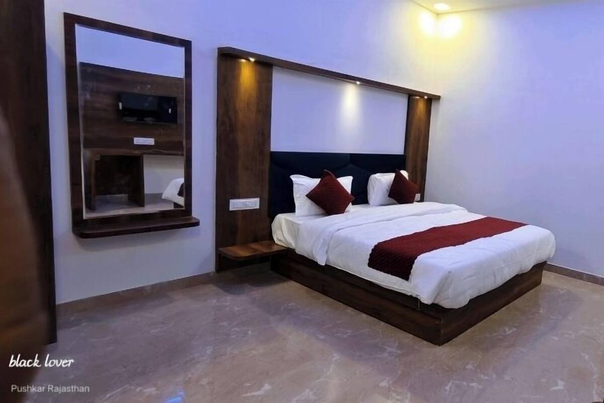 A bedroom with a large bed, wooden headboard, a mirror, and a TV mounted on the wall.