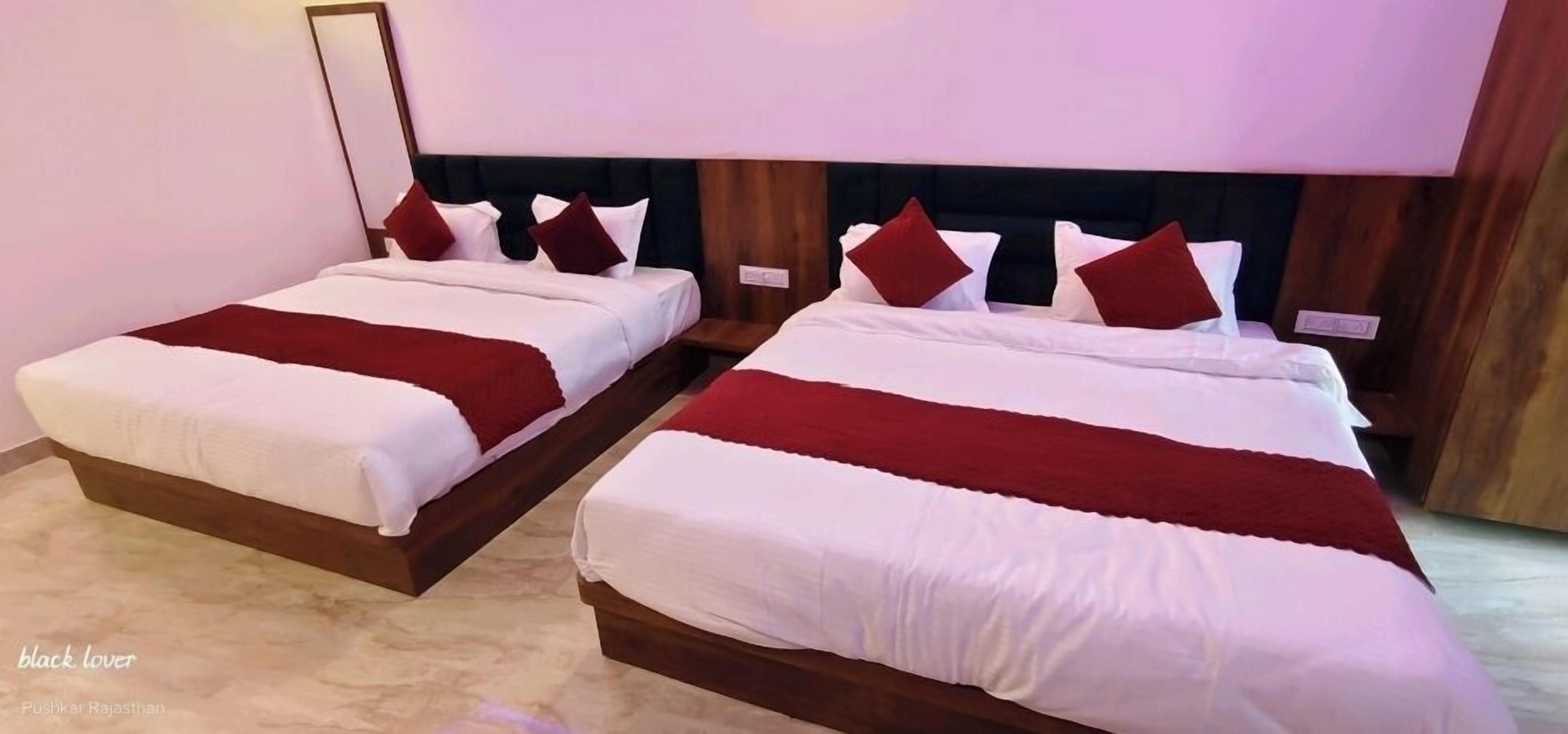 Two double beds with white and red bedding, wooden headboards, and a marble floor.