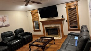 A living room with a fireplace, black leather sofas, a coffee table, and a ceiling fan.