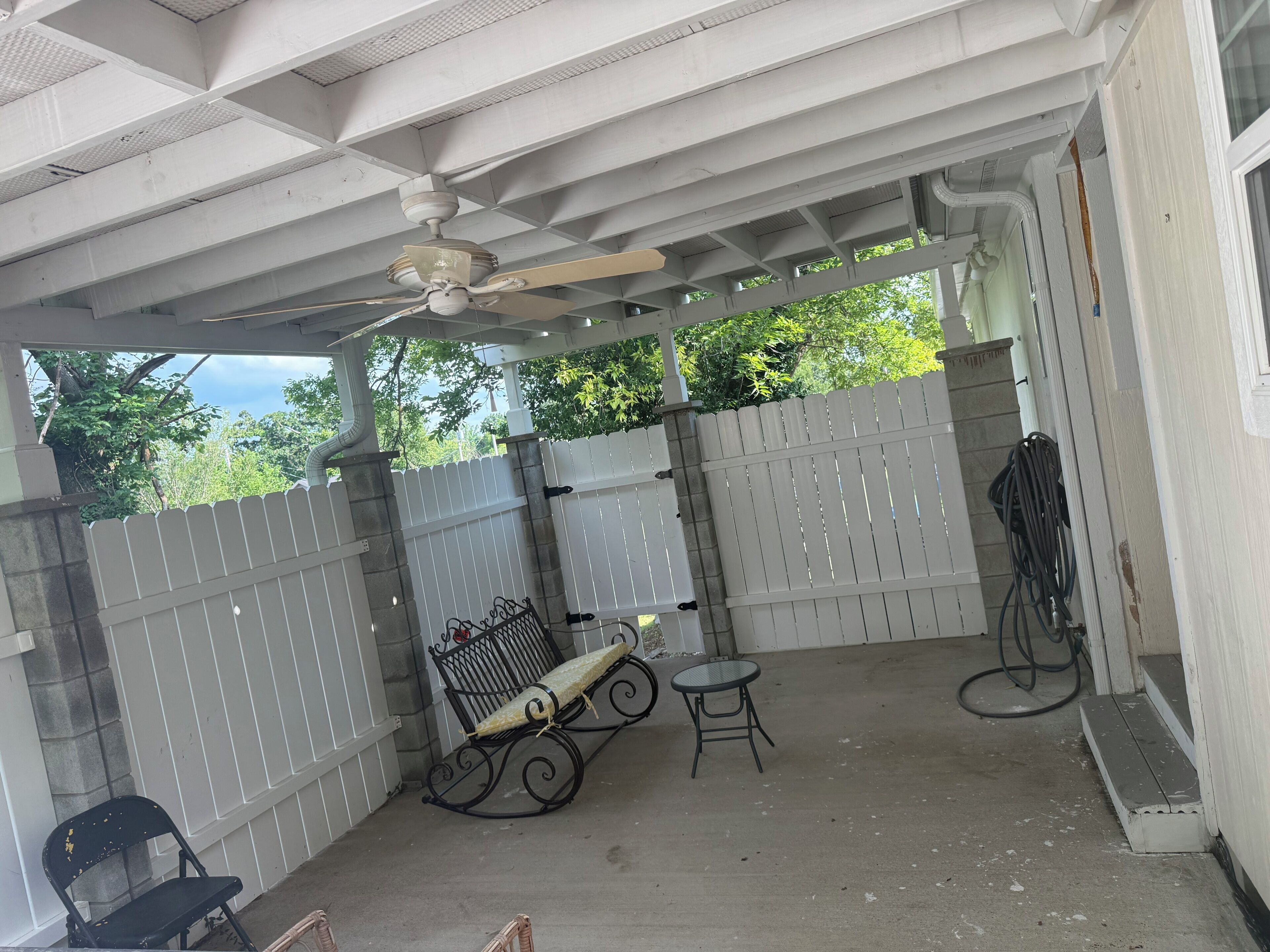Un patio couvert avec un ventilateur de plafond, un banc, une petite table et une chaise.