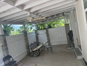 En overdækket terrasse med ventilator, bænk, lille bord og stol.