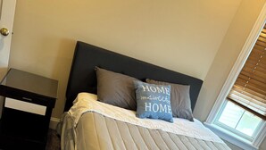 A neatly made bed with a beige and white striped bedspread, two pillows, and a small bedside table with a lamp.