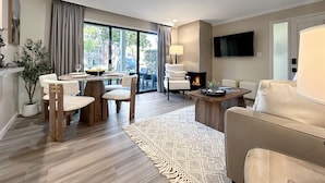 A modern living room with a fireplace, a dining area with wooden chairs, and a large window providing a view of the outdoors. - Stylish Napa Retreat | Patio • W/D • 10 Min to DT (Napa)
