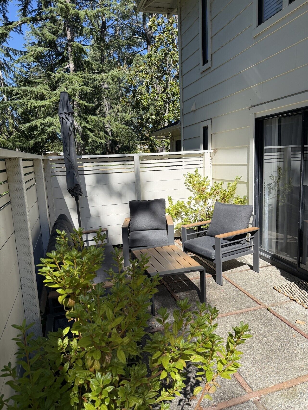 An outdoor patio with two chairs and a table, surrounded by a white fence and greenery.