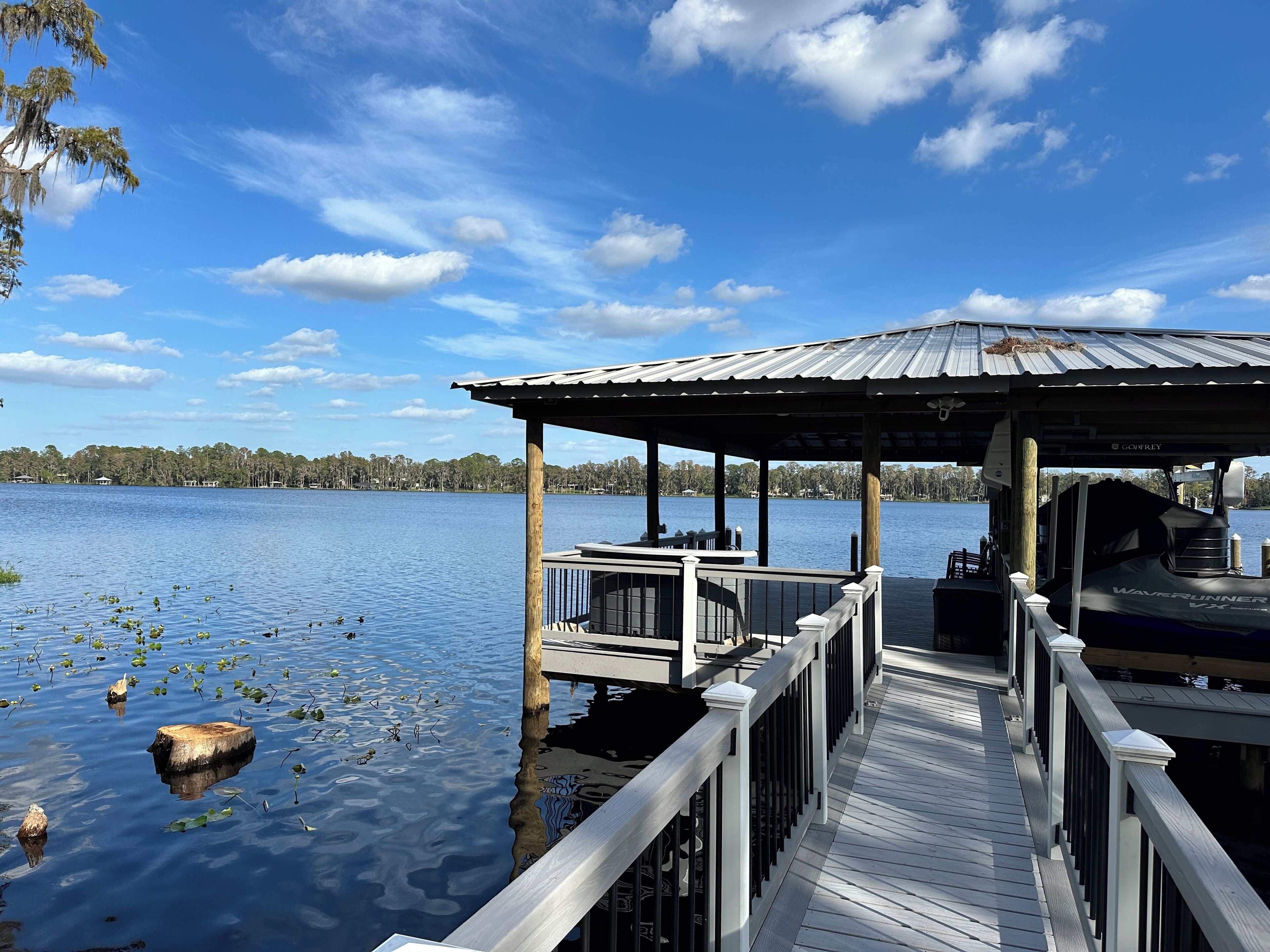 A wooden dock extending into a calm lake with a gazebo and a boat named 'Waverunner VX' on the right.