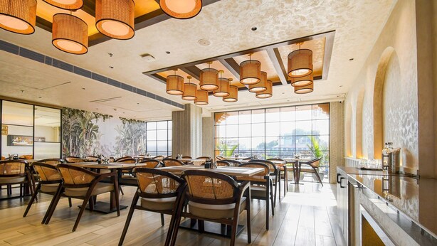 A spacious dining area with multiple tables and chairs, large windows offering a view, and modern pendant lighting.
