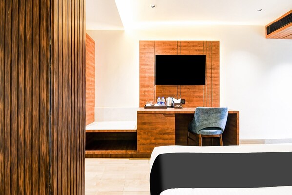A modern hotel room with a wooden desk, a flat-screen TV, a bed, and a chair. - Deluxe Double Stays Near Paridh Crossing (Golmuri)