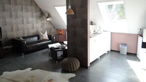 Ein modernes Wohnzimmer mit einer Couch, einem Couchtisch und einem Teppich. Es gibt eine Küchenzeile mit einer Spüle und Schränken.