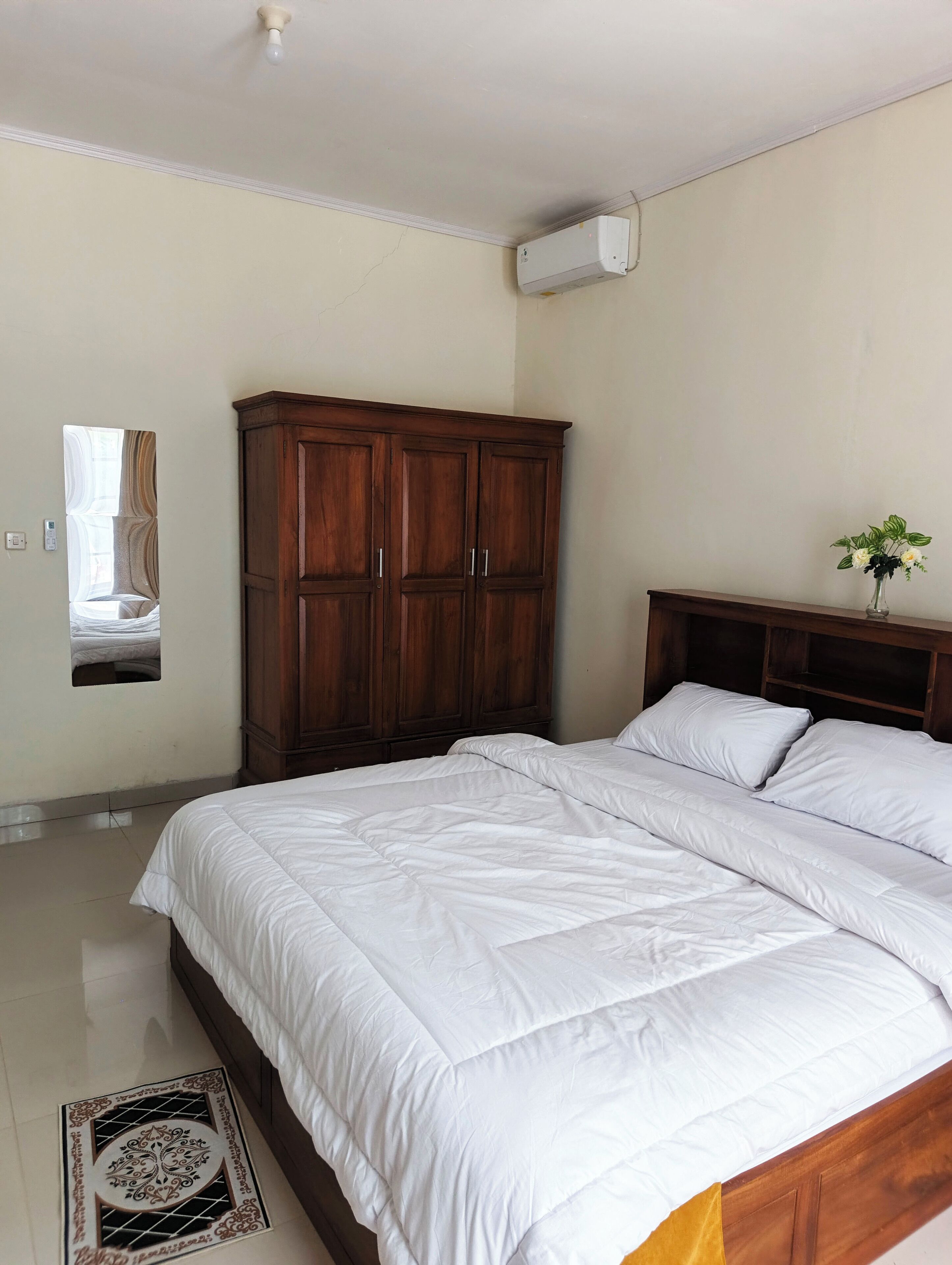 A bedroom with a large bed, wooden wardrobe, and a mirror on the wall.