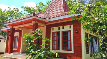 Uma casa de dois andares com telhado de telhas vermelhas, paredes de tijolo e janelas grandes com molduras brancas.