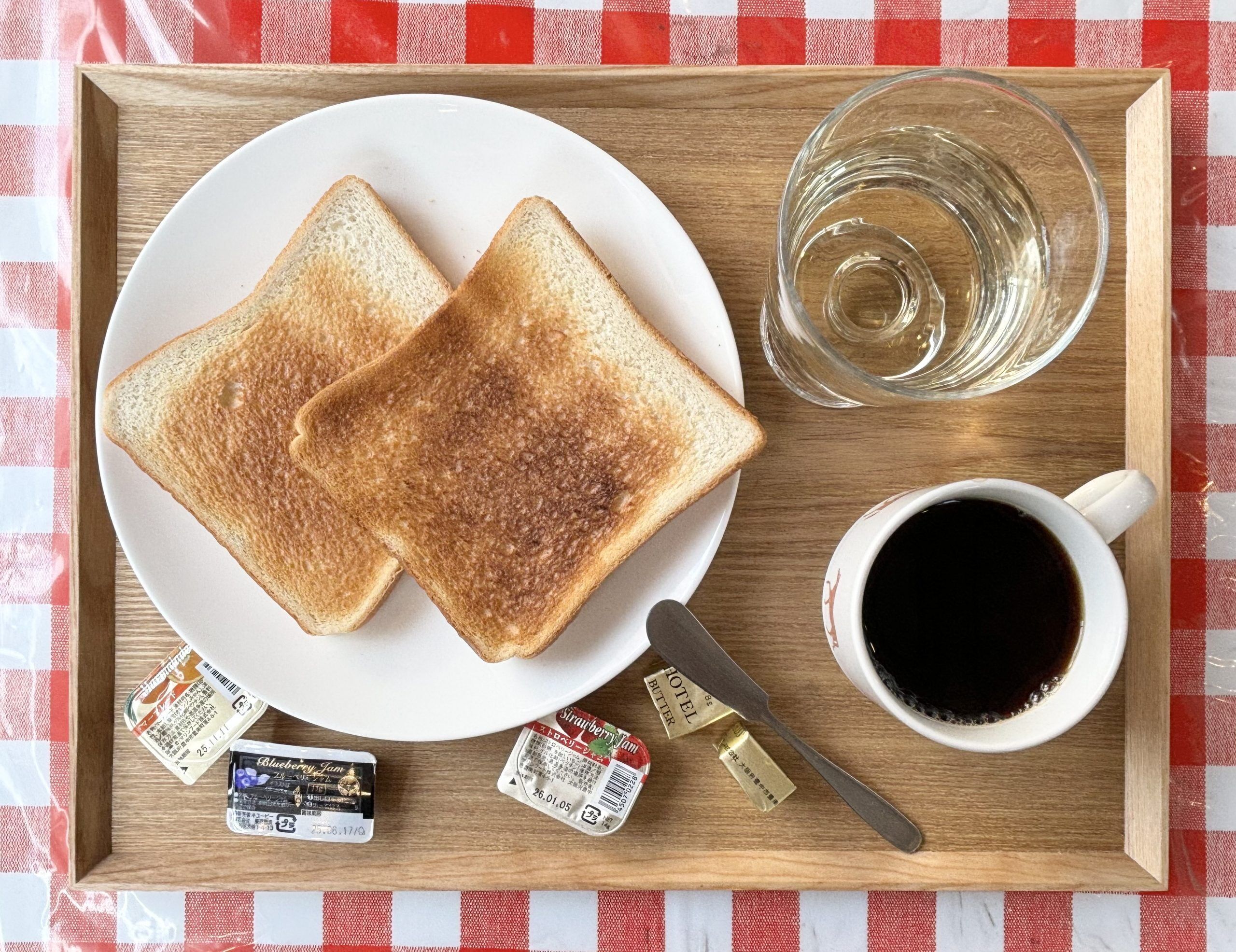 A tray with two slices of toast, a glass of water, a cup of coffee, and some condiments.