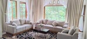 A living room with two beige sofas, a black coffee table, and a patterned rug. - Amini Guest House (Karangmojo)