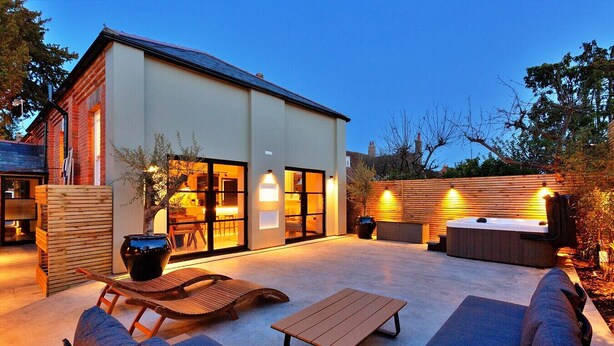 Ein modernes Haus mit einer Terrassenanlage, die Gartenmöbel, ein Whirlpool und ein großes Fenster mit Blick auf den Garten bietet.