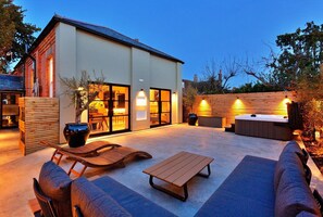 Une maison moderne dotée d’un patio aménagé avec du mobilier d’extérieur, un jacuzzi et une grande fenêtre donnant sur le jardin.