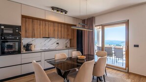 Una cocina moderna con salpicadero de mármol, armarios de madera y una zona de comedor con mesa y sillas de vidrio.