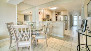 A modern kitchen with a central island, dining area with chairs, and a refrigerator.