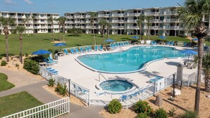 A hotel pool area with a large pool, sun loungers, and a hot tub.