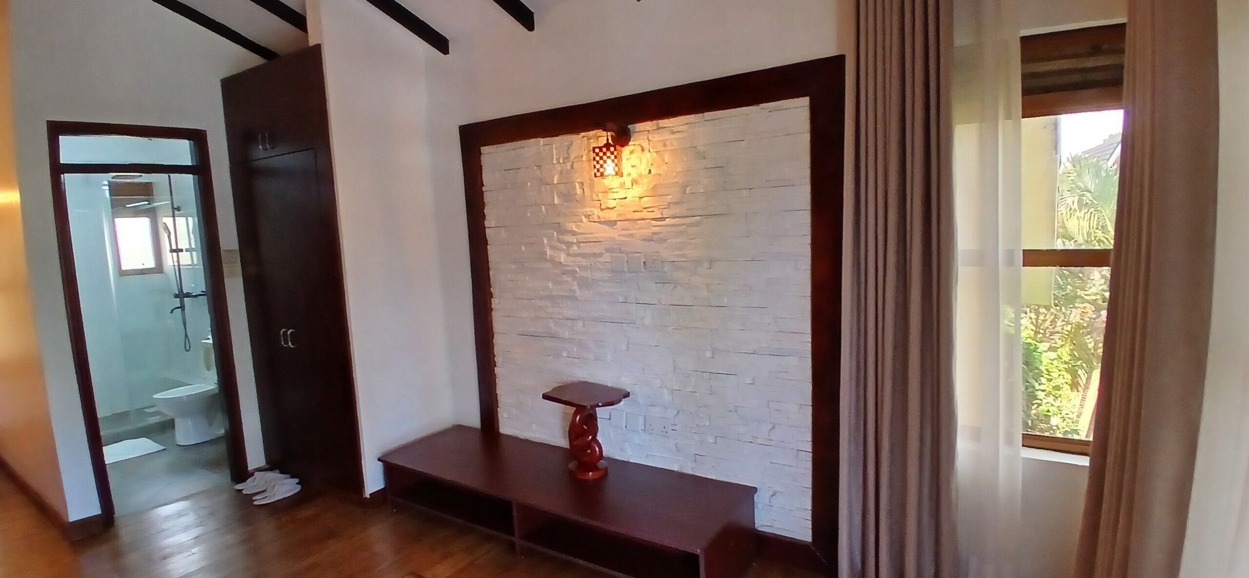 A room with a wooden bench, a white brick wall, and a window with curtains.