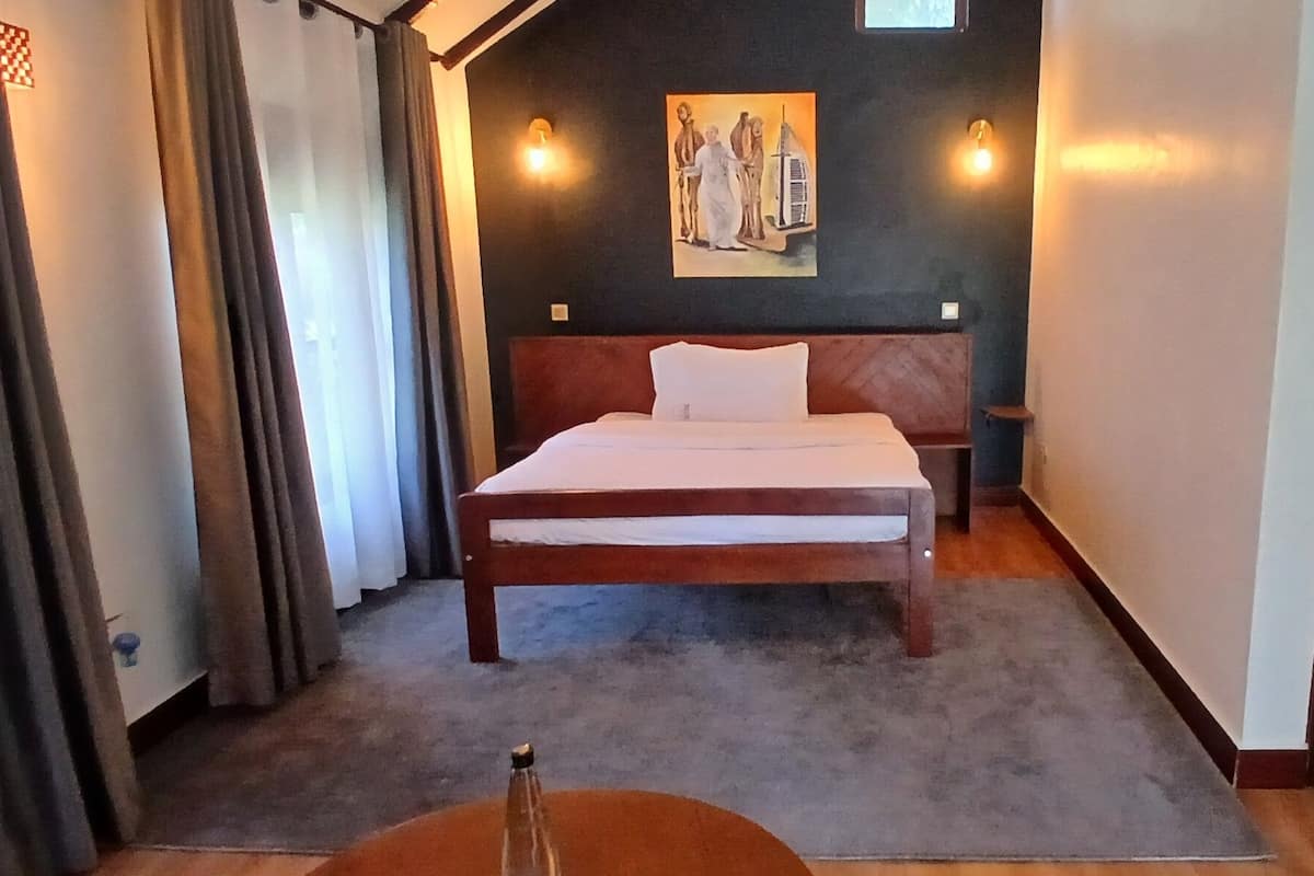 A hotel room with a bed, a painting on the wall, and a bathroom visible through an open door.