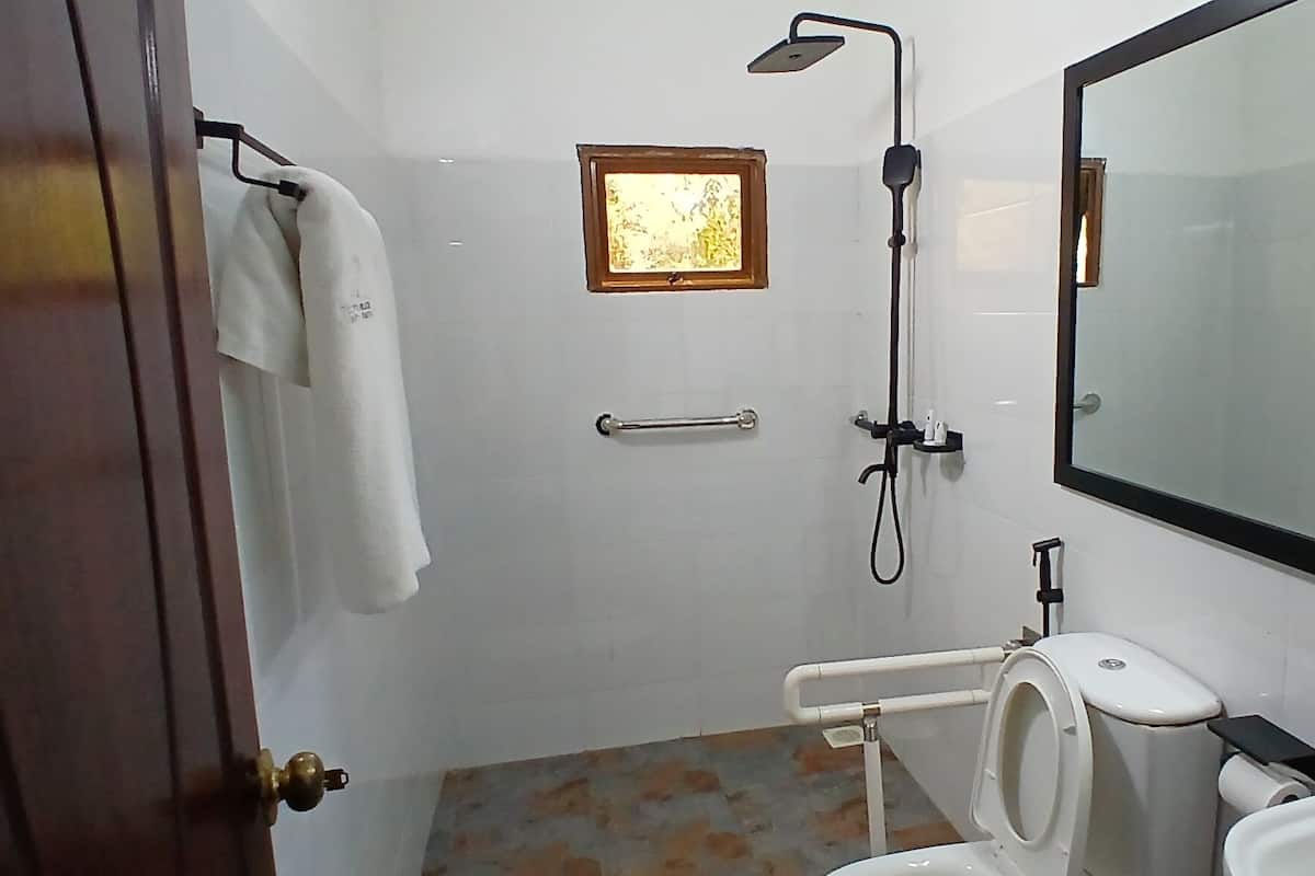 A bathroom with a toilet, sink, mirror, shower, and a small window.