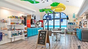 Un restaurant moderne offrant une vue sur l’océan, avec un menu écrit à la craie, un espace de libre-service et divers plats présentés sur des étagères.