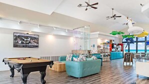 Un vaste espace de vie comprenant une table de billard, un canapé de couleur turquoise et un coin bar offrant une vue sur l’océan.