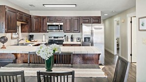 Une cuisine moderne avec des meubles en bois foncé, des appareils électroménagers en acier inoxydable et un îlot central agrémenté d’un vase de fleurs.