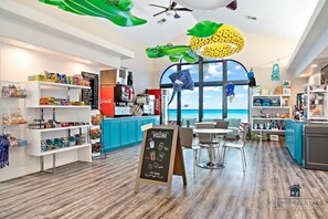 Um restaurante moderno com vista para o mar, com cardápio em lousa, estação de autoatendimento e diversos alimentos expostos em prateleiras.