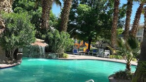 A swimming pool surrounded by palm trees and greenery, with lounge chairs and a water feature. - Top-Floor Condo with Pools, Water Slides, Hot Tub! (St. George)