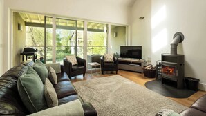A living room with a sofa, TV, fireplace, and large windows. - Beaverbrook Lodge | Family | Spa | Pool Access (Somerford Keynes)