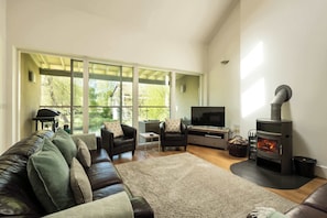 A living room with a sofa, TV, fireplace, and large windows. - Beaverbrook Lodge | Family | Spa | Pool Access (Somerford Keynes)