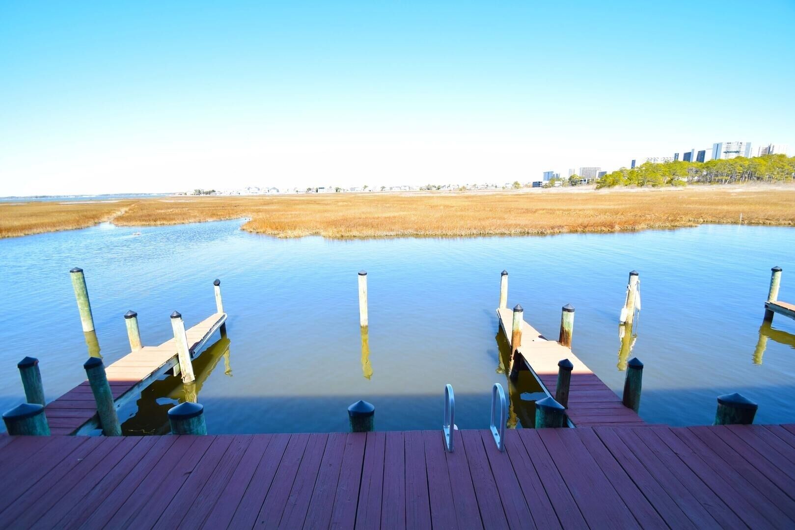 Une jetée en bois s’étendant sur une étendue d’eau calme, offrant une vue dégagée sur les contours d’une ville lointaine.