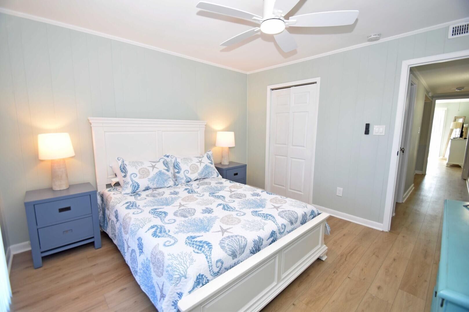 A bedroom with a bed, nightstands, a ceiling fan, and a door.