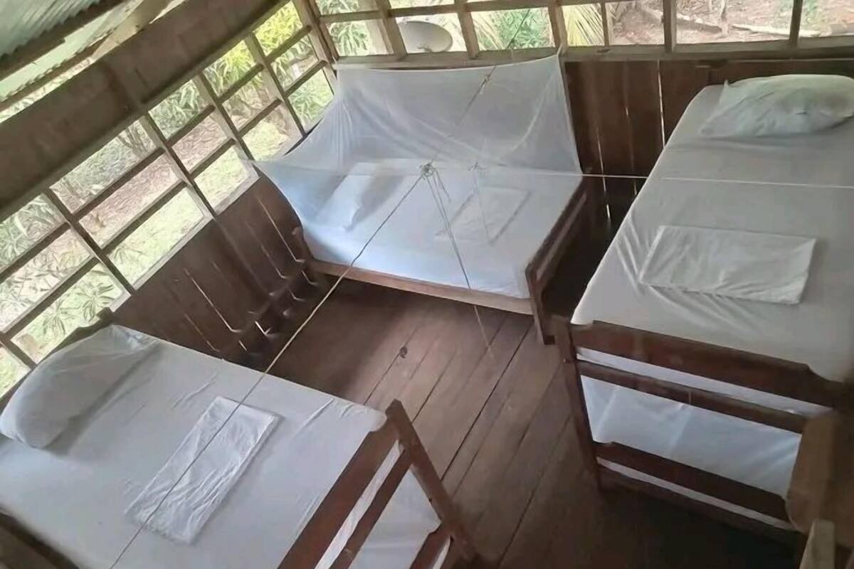 Una habitación con tres camas de madera, cada una con ropa blanca y estructura de madera.