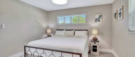 A bedroom with a bed, bedside tables, a window, and wall art.