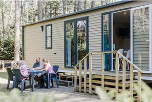 A small cabin with a deck and a table where a family is seated. - Peaceful Woodland Chalet (Lille)
