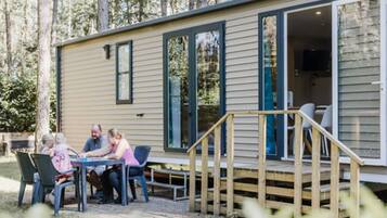 A small cabin with a deck, a dining area with chairs, and a staircase leading to the entrance.