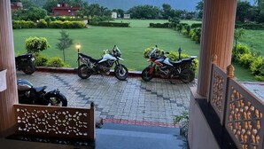 A view from a balcony overlooking a well-maintained lawn with two motorcycles parked on the pavement. - The Dhawala Resort (Alwar)