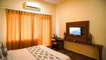 Una habitación de hotel con cama, escritorio, televisor y aire acondicionado.