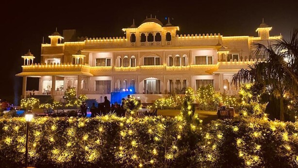 A large, illuminated building with multiple balconies and arched windows, surrounded by well-lit bushes. - The Dhawala Resort (Alwar)