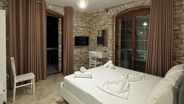 Une chambre avec un mur en pierre, un lit avec du linge de lit blanc, un bureau et une chaise.