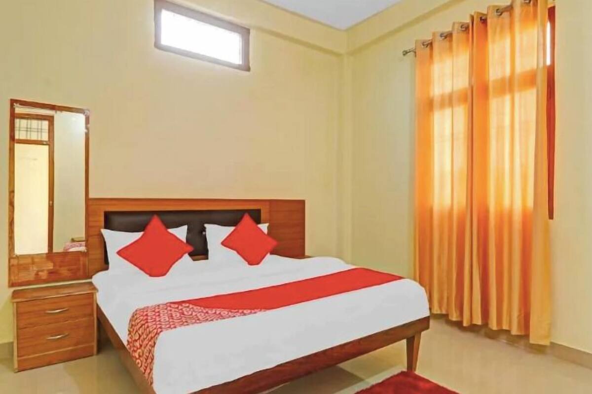 A hotel room with a bed, a nightstand, a mirror, and a window with curtains.