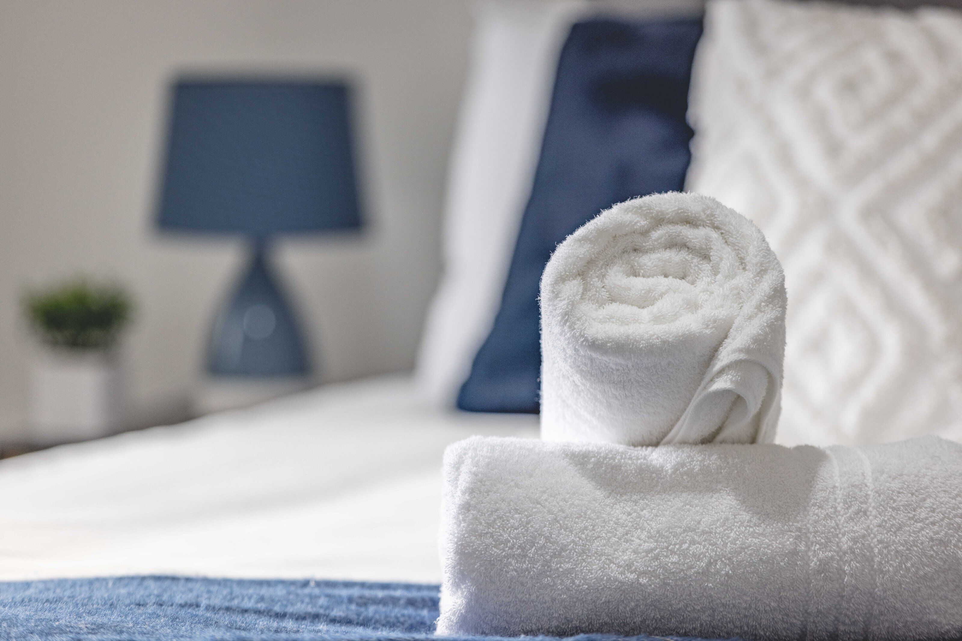 Un lit bien fait, avec une serviette blanche roulée placée au premier plan, un oreiller bleu et un oreiller à motifs en arrière-plan.