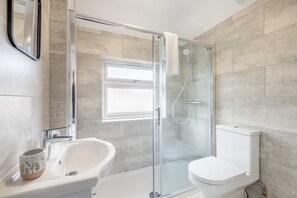 Un baño moderno con ducha de vidrio, lavamanos blanco y un inodoro.
