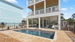 A two-story building with a covered outdoor swimming pool area, a fenced patio, and a view of a blue building in the background.